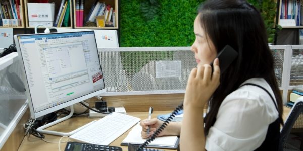 A worker is talking on the phone and sitting in front of the computer.